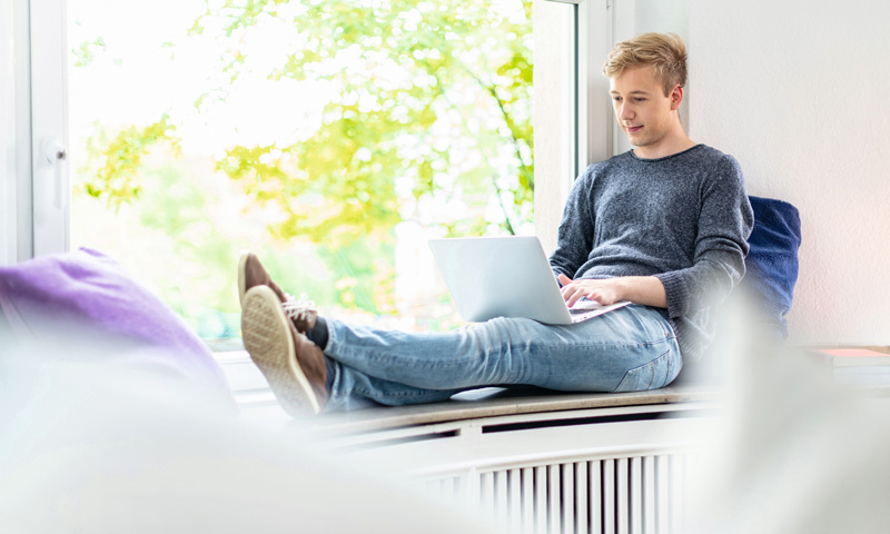 Studierender am Laptop auf einer Fensterbank